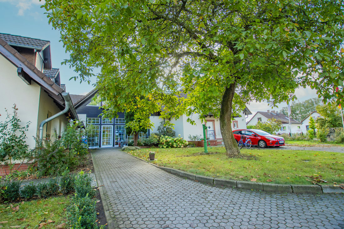 Eine Auffahrt mit Bäumen und ein Haus mit einem roten Auto, das hinten geparkt ist.